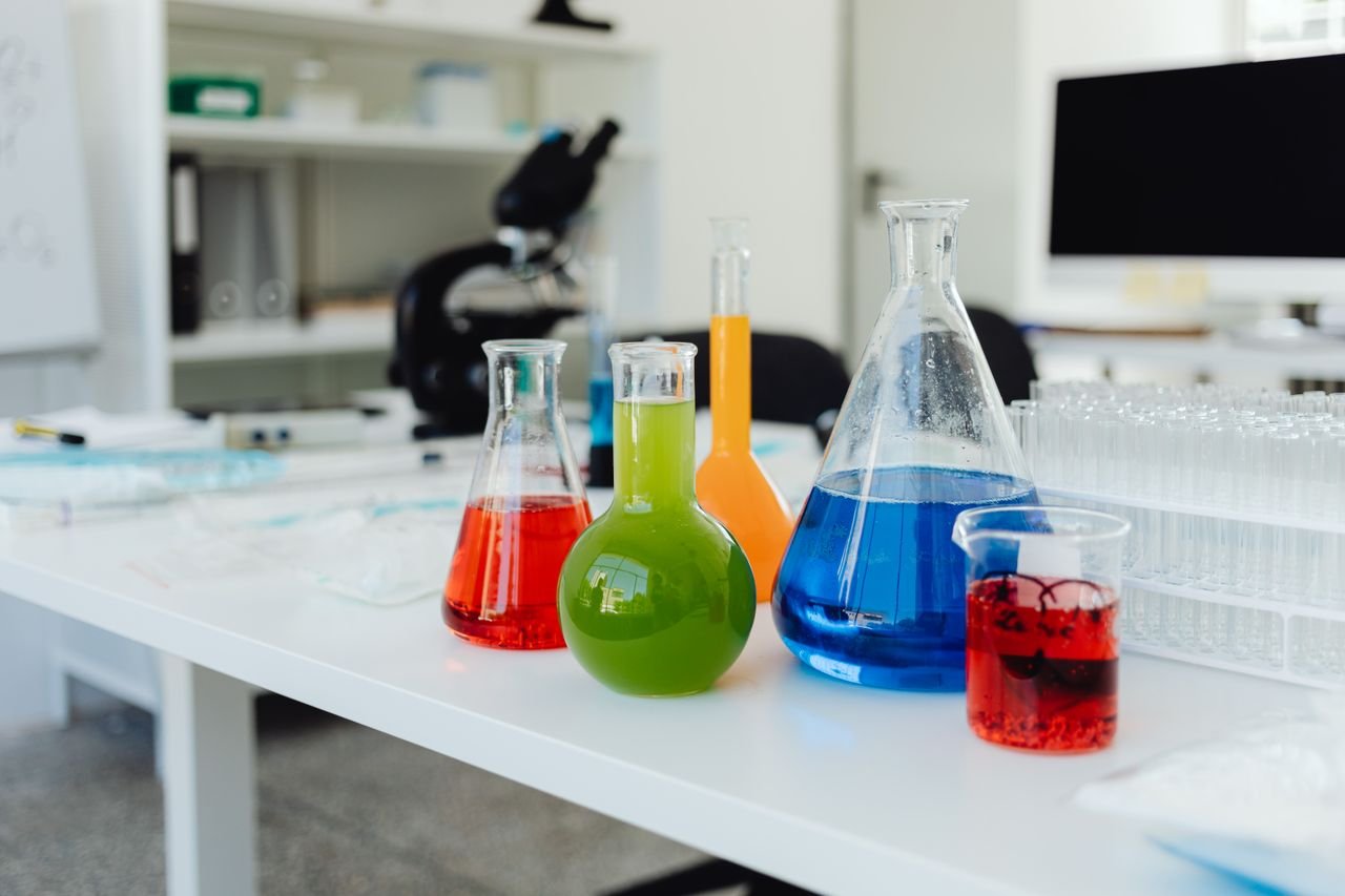 Home Bright, colorful chemicals in flasks and beakers on a lab table indicating a chemistry experiment in progress.